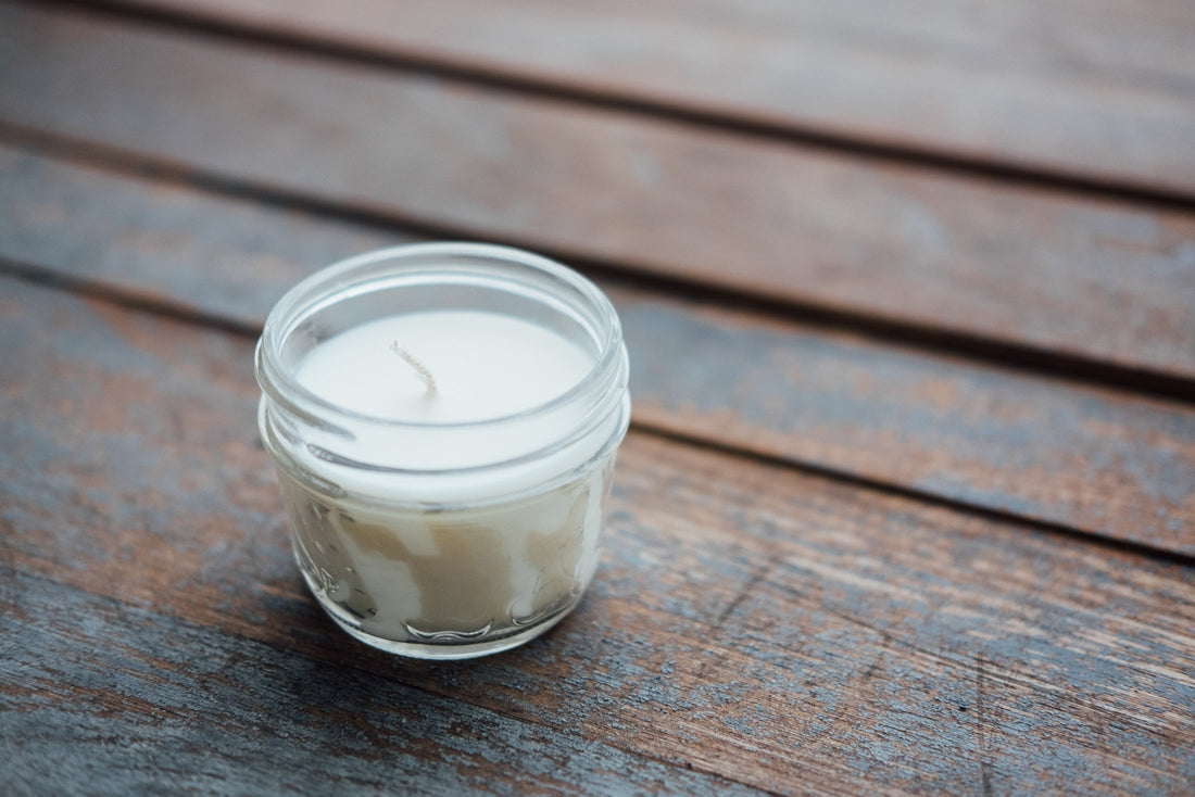 glass jar white candle sitting on a wooden table