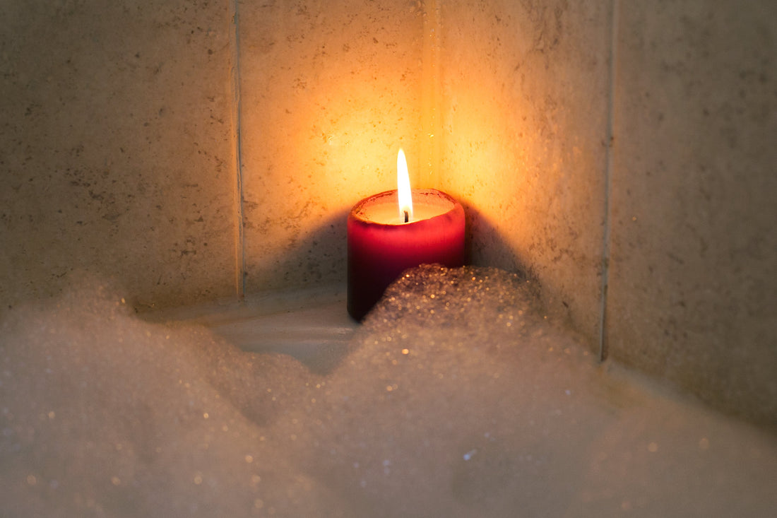 Lit candle sitting in the corner of a bath tub with bubbles
