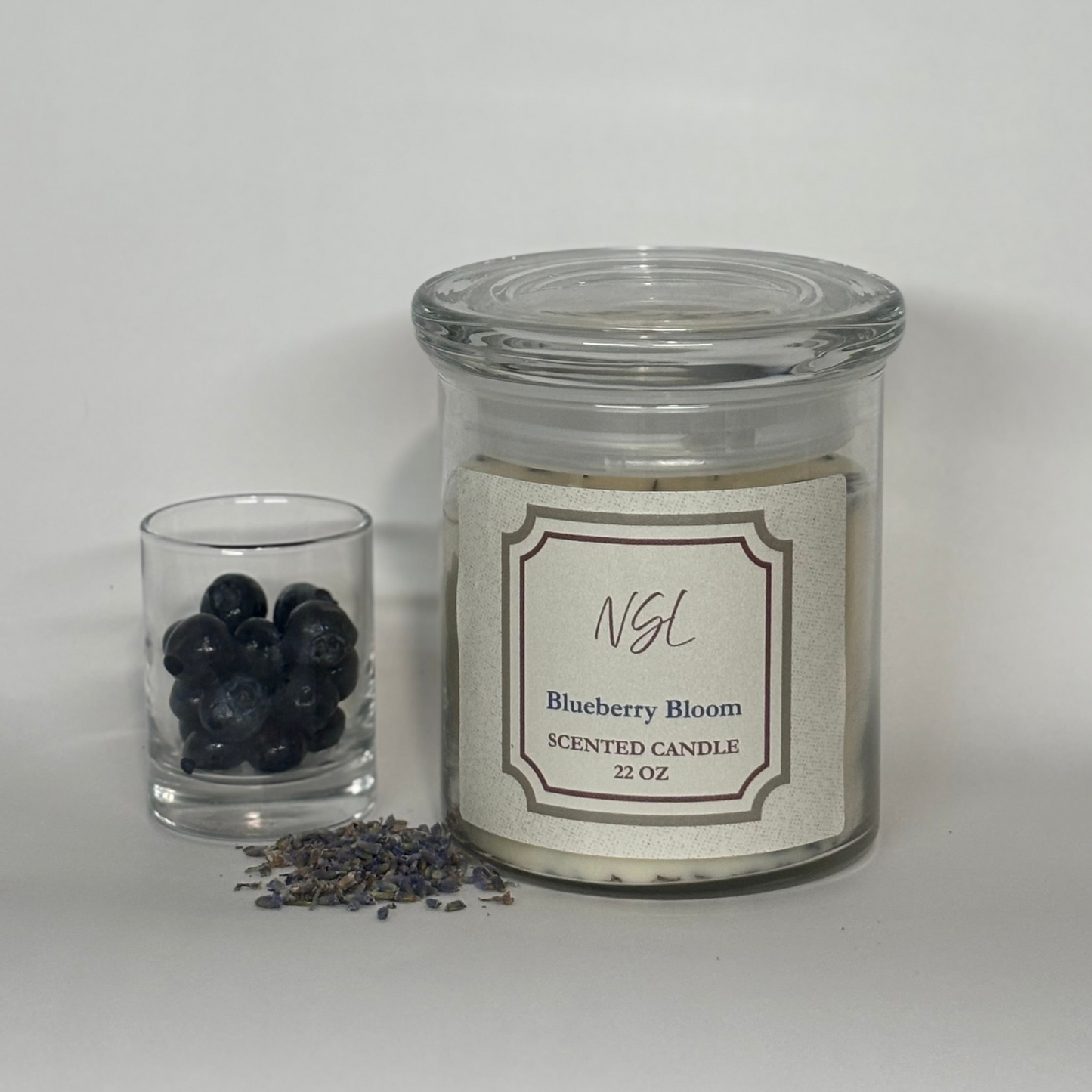Scented candle labeled 'Blueberry Bloom' with a small glass container of blueberries and lavender on a white background