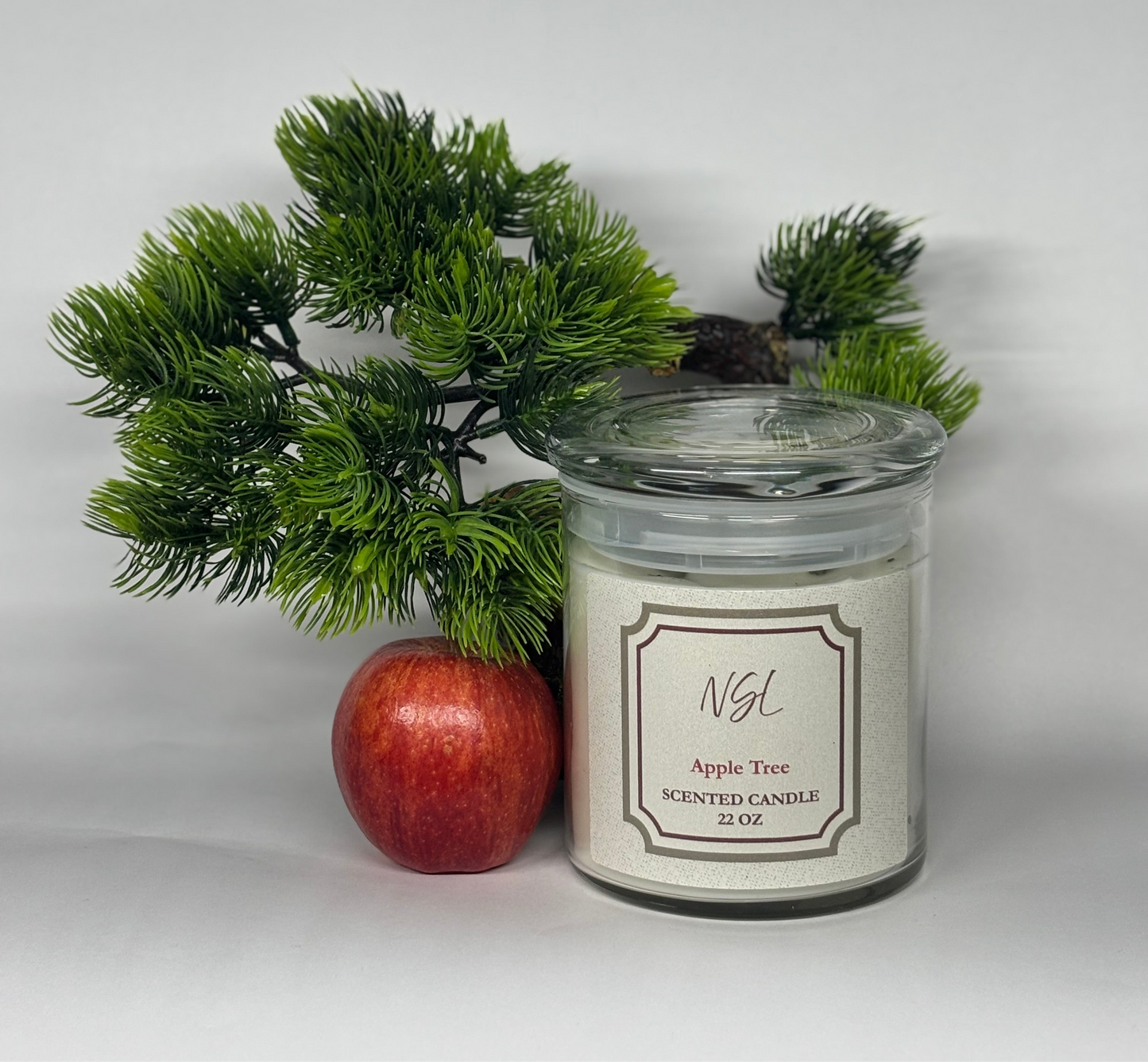 22oz wood wick apple tree candle with a white background next to a tree and apple.